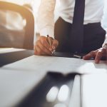 Business man in white shirt leaning onto table with pen in hand